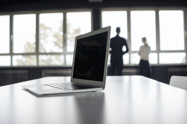 Laptop auf dem Tisch und Geschäftsmann und Geschäftsfrau am Fenster - JOSF01504