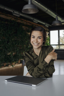 Porträt einer lächelnden jungen Frau im Büro mit Laptop - JOSF01507