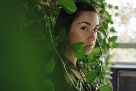 Portait of young woman at wall with climbing plants stock photo