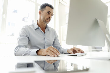 Businessman using computer at desk in office - KNSF02441