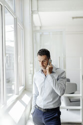 Businessman at the window in office on cell phone - KNSF02449
