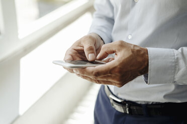 Close-up of businessman at the window using cell phone - KNSF02451