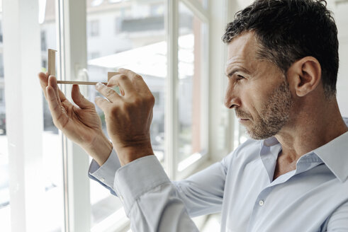 Geschäftsmann am Fenster mit Blick auf ein Architekturmodell - KNSF02453