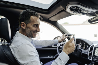 Businessman driving car looking at cell phone - KNSF02470