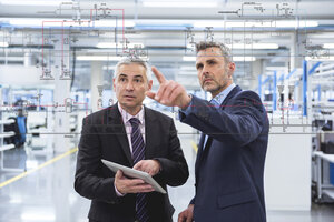 Two businessmen looking at graphic on glass pane in factory hall - DIGF02771