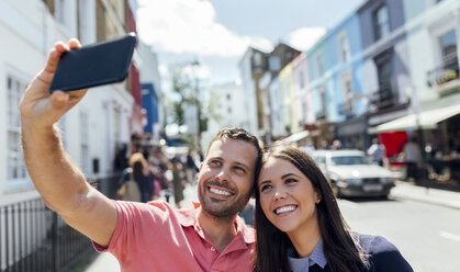 UK, London, Portobello Road, glückliches Paar macht Selfie mit Handy - MGOF03578