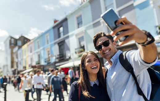 UK, London, Portobello Road, Porträt eines lachenden Paares, das ein Selfie mit einem Smartphone macht - MGOF03581