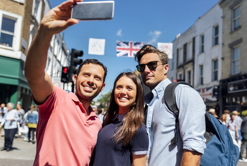 UK, London, Portobello Road, Porträt von drei Freunden, die ein Selfie mit einem Smartphone machen - MGOF03595