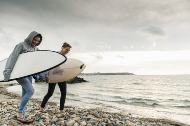 Happy friends with surfboard walking on stony beach - UUF11636