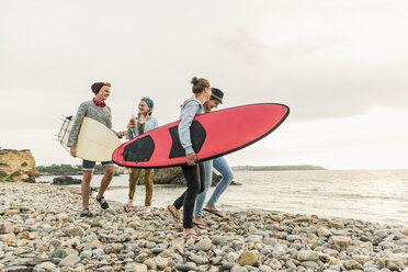 Happy friends with surfboards walking on stony beach - UUF11637