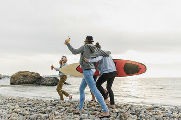 Happy friends with surfboards walking on stony beach - UUF11638