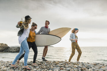 Happy friends with surfboards walking on stony beach - UUF11639