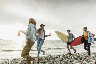 Happy friends with surfboards walking on stony beach - UUF11642