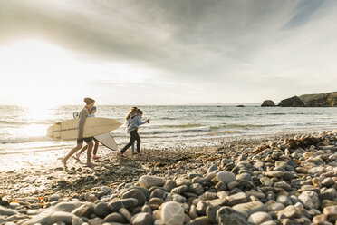 Happy friends with surfboards walking on stony beach - UUF11644