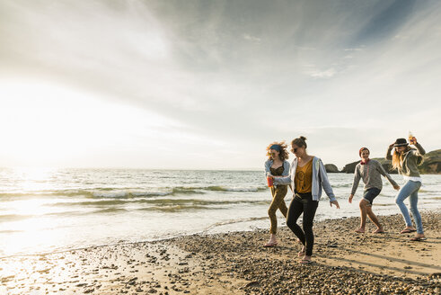 Glückliche Freunde, die bei Sonnenuntergang am Strand spazieren gehen - UUF11651