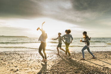 Happy friends walking on the beach at sunset - UUF11652