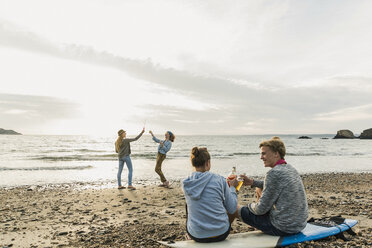 Glückliche Freunde mit Surfbrett und Getränken am Strand bei Sonnenuntergang - UUF11660