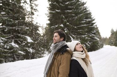 Happy young couple standing back to back in snow-covered winter landscape - HAPF02033