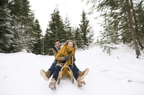 Glückliches junges Paar auf Schlitten im Winterwald - HAPF02043