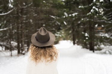 Back view of young woman wearing hat and knit pullover in winter forest - HAPF02052