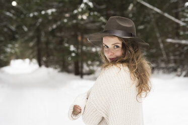 Portrait of smiling young woman wearing hat and knit pullover in winter forest - HAPF02053