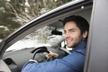 Porträt eines lächelnden jungen Mannes beim Autofahren im Winter - HAPF02063