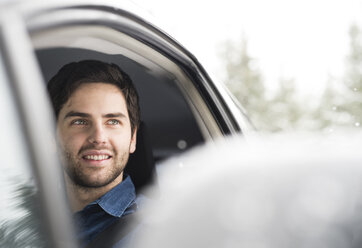 Porträt eines lächelnden jungen Mannes beim Autofahren im Winter - HAPF02070
