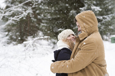 Happy young couple standing face to face in snow-covered winter forest - HAPF02071