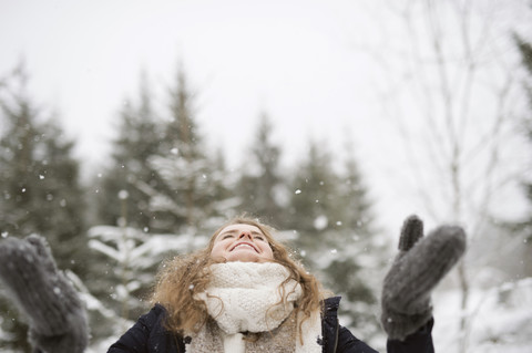 Glückliche junge Frau genießt den Schneefall im Winterwald, lizenzfreies Stockfoto