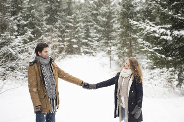 Glückliches junges Paar, das Hand in Hand in einer Winterlandschaft steht und sich gegenseitig anschaut - HAPF02081