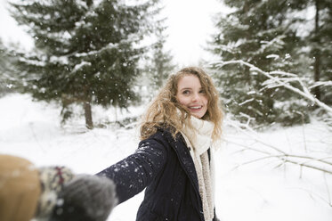Porträt einer glücklichen jungen Frau, die im Winterwald ihre Hand hält - HAPF02084