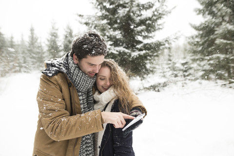 Glückliches junges Paar steht im verschneiten Winterwald und telefoniert, lizenzfreies Stockfoto