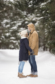 Glückliches junges Paar, das in einer verschneiten Winterlandschaft von Angesicht zu Angesicht steht - HAPF02091