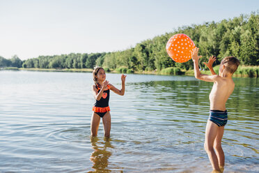 Junge und Mädchen stehen am Seeufer und spielen mit einem Wasserball - MJF02181