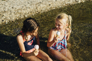 Zwei Mädchen sitzen im Wasser am Seeufer und essen Eis - MJF02185