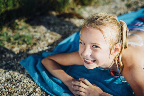 Portrait of smiling blond girl lying on towel on the beach - MJF02192
