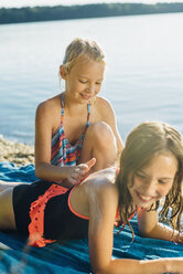 Mädchen trägt Sonnencreme auf die Schulter ihres Freundes am Strand auf - MJF02194