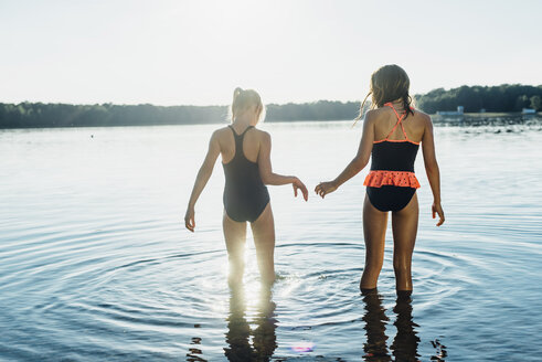 Rückenansicht von zwei Freunden in Badeanzügen, die am Seeufer stehen - MJF02200