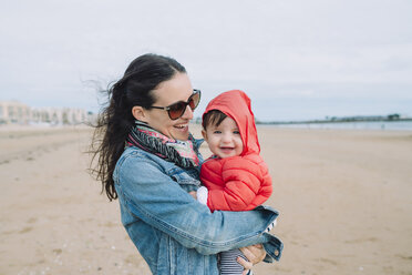 Portrait of smiling baby girl on her mother's arms on the beach - GEMF01773