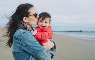 Portrait of smiling baby girl on her mother's arms on the beach - GEMF01775