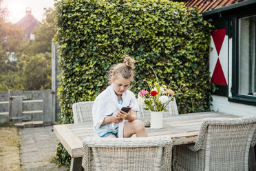 Girl sitting on terrace table using cell phone - MOEF00066