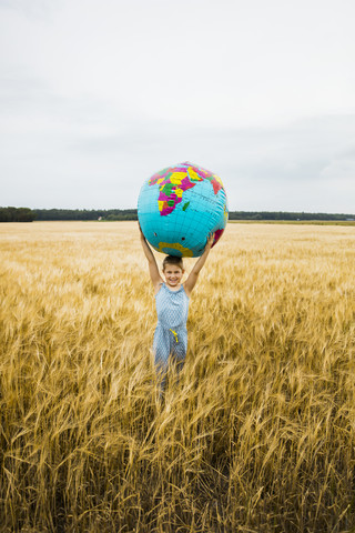 Mädchen steht in einem Getreidefeld und hält einen Globus, lizenzfreies Stockfoto