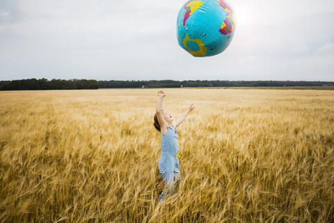 Mädchen steht in einem Getreidefeld und spielt mit einem Globus, lizenzfreies Stockfoto