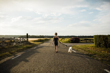 Mädchen, das mit seinem Hund auf einer Landstraße spazieren geht und ein Miniatur-Windrad hält - MOEF00094