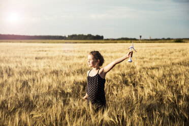 Girl standing in grain field holding miniature wind turbine - MOEF00096
