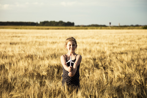 Mädchen steht in einem Getreidefeld und hält ein Miniatur-Windrad, lizenzfreies Stockfoto