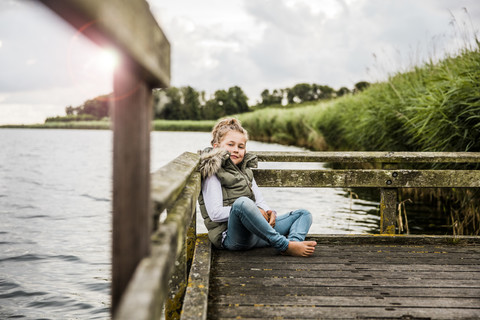 Mädchen sitzt auf einem Steg an einem See, lizenzfreies Stockfoto