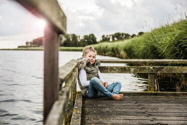 Mädchen sitzt auf einem Steg an einem See - MOEF00104