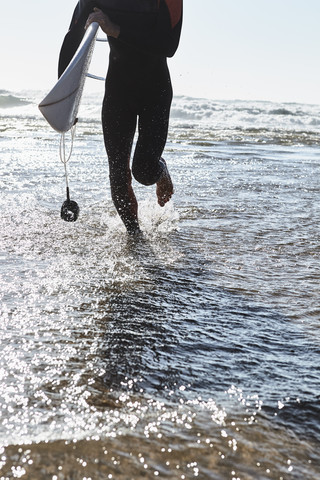 Portugal, Algarve, Mann läuft mit Surfbrett im Wasser, lizenzfreies Stockfoto