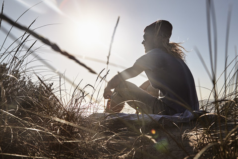 Portugal, Algarve, Mann sitzt bei Sonnenuntergang am Strand, lizenzfreies Stockfoto